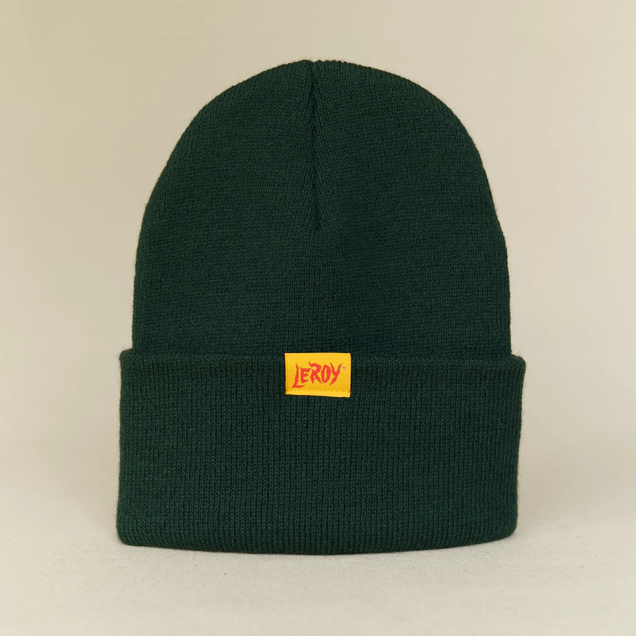A hunter green knit beanie with a small rectangular woven label reading 'LEROY' in red and orange lettering on a yellow background.