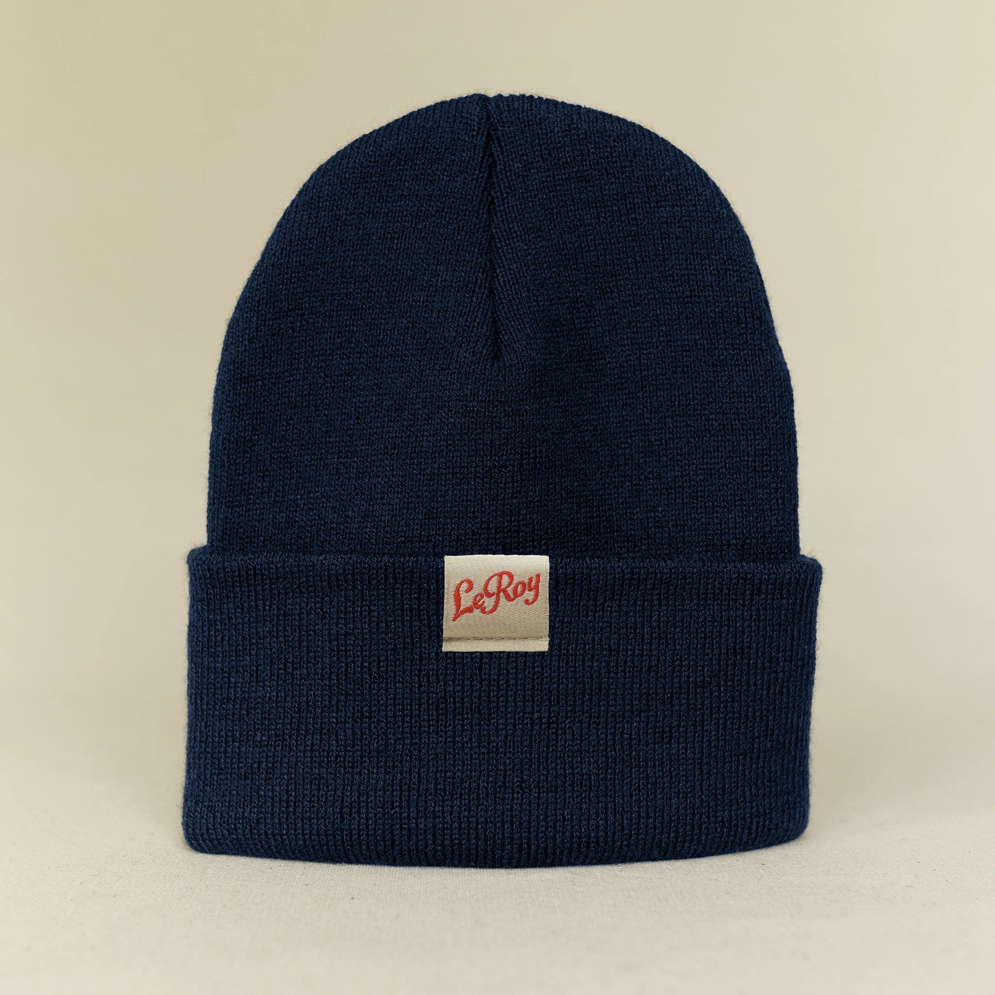 A navy blue knit beanie with a small rectangular woven label reading 'LeRoy' in red script on a light background.