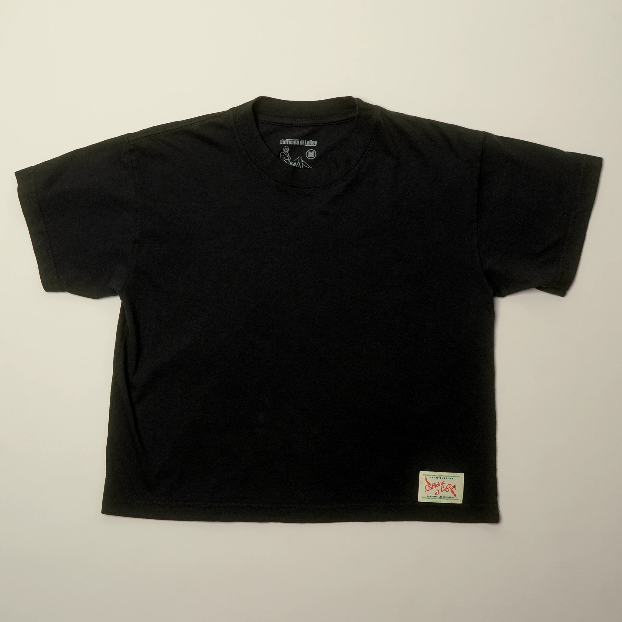 A single black t-shirt laid flat on a light background, showing a small woven label on the bottom right.