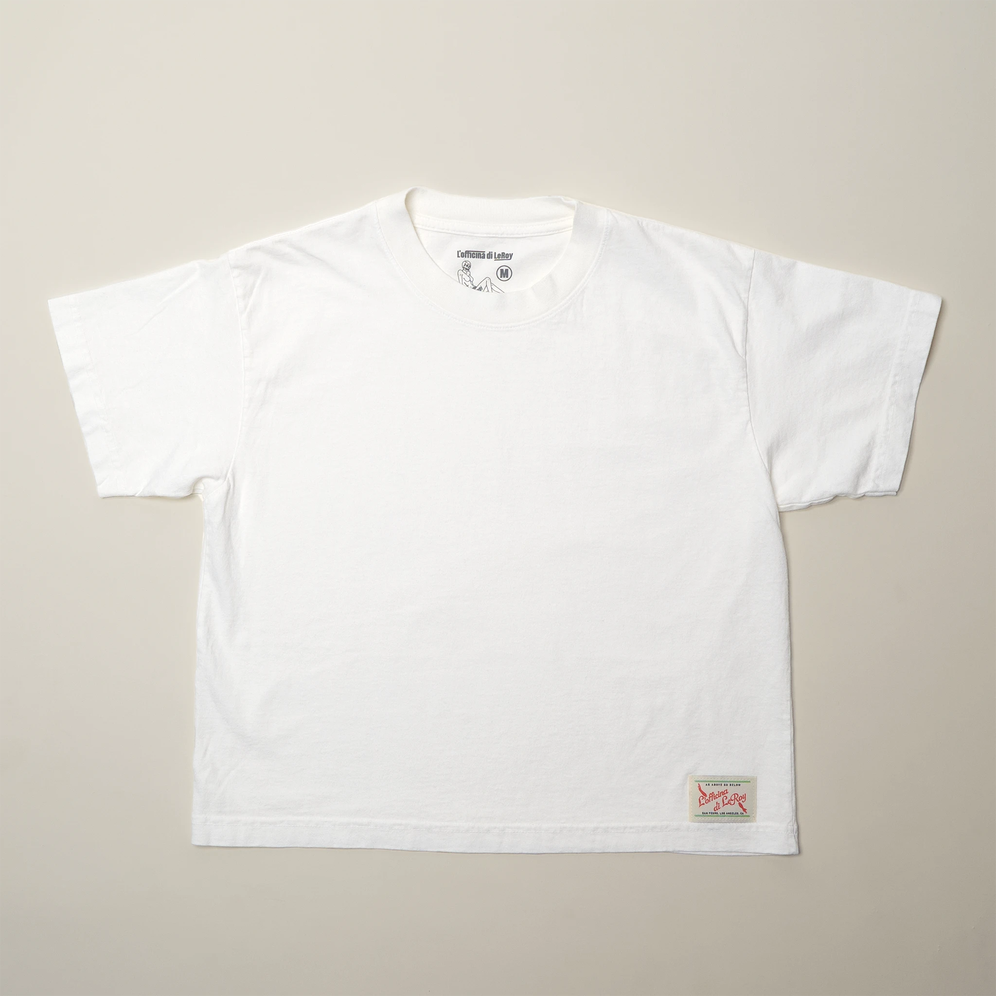 A single white t-shirt laid flat on a light background, showing a small woven label on the bottom right.