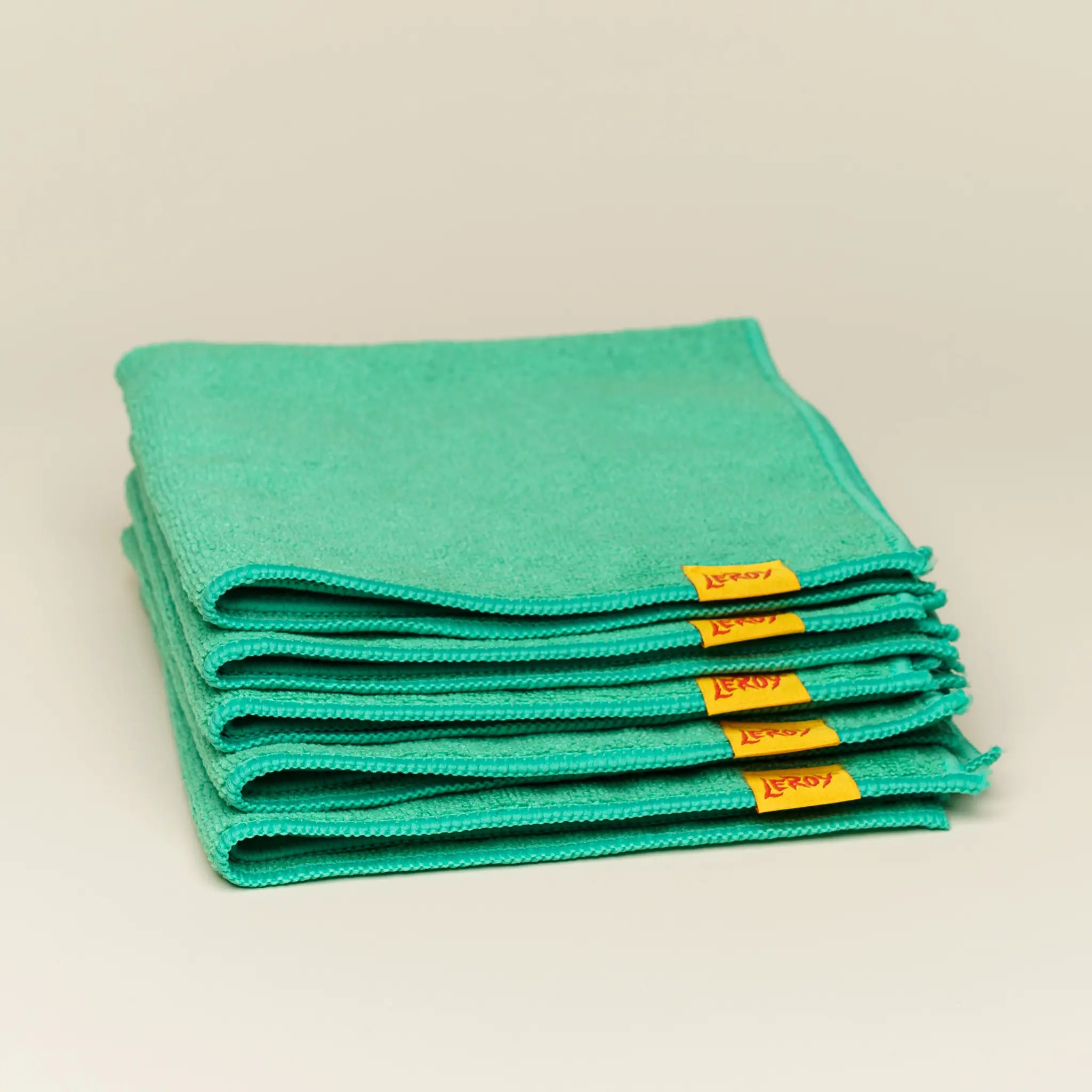 A stack of five folded green microfiber towels on a light background, each with a small yellow label reading 'LEROY' in red letters.