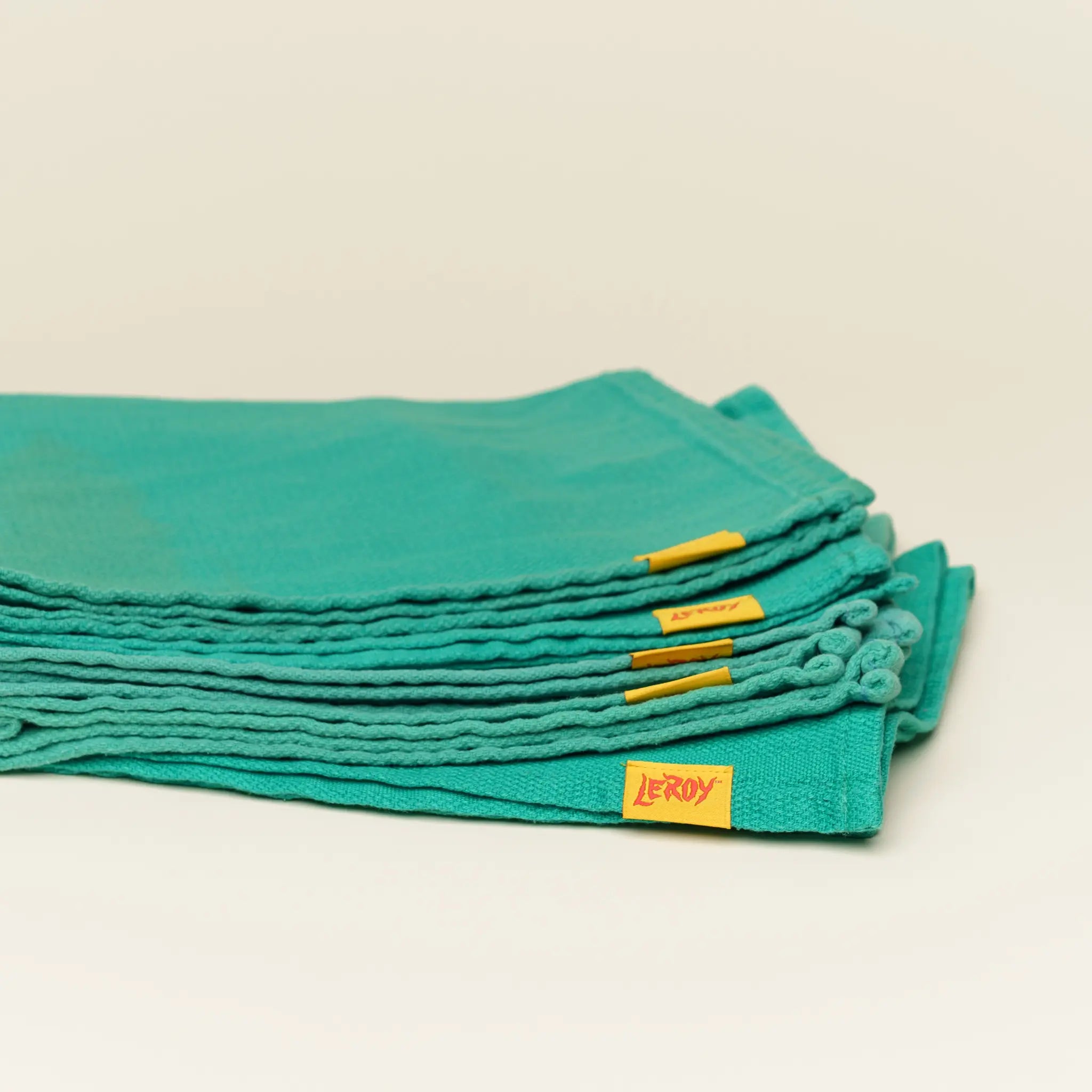 A stack of folded, reclaimed green huck towels on a light background, each featuring a small yellow label with 'LEROY' in red lettering.